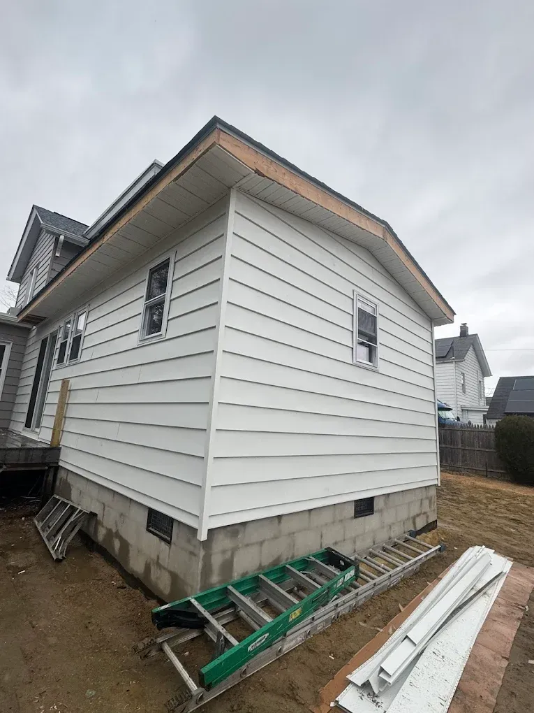 White house exterior with horizontal siding, concrete foundation, and ladders on muddy ground beside it