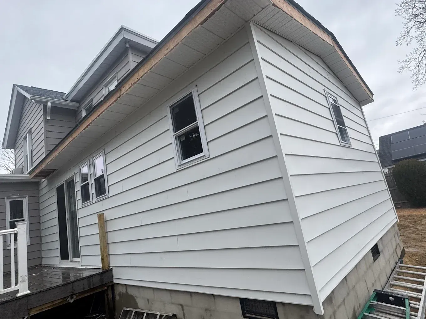 Side view of a white vinyl-sided house with open windows and a raised deck, under cloudy skies