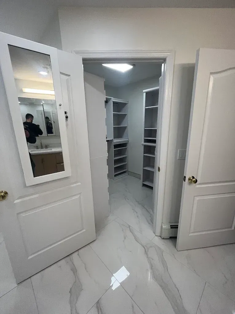 Open double doors to a bright walk-in closet with white shelves and glossy marble-patterned floor.