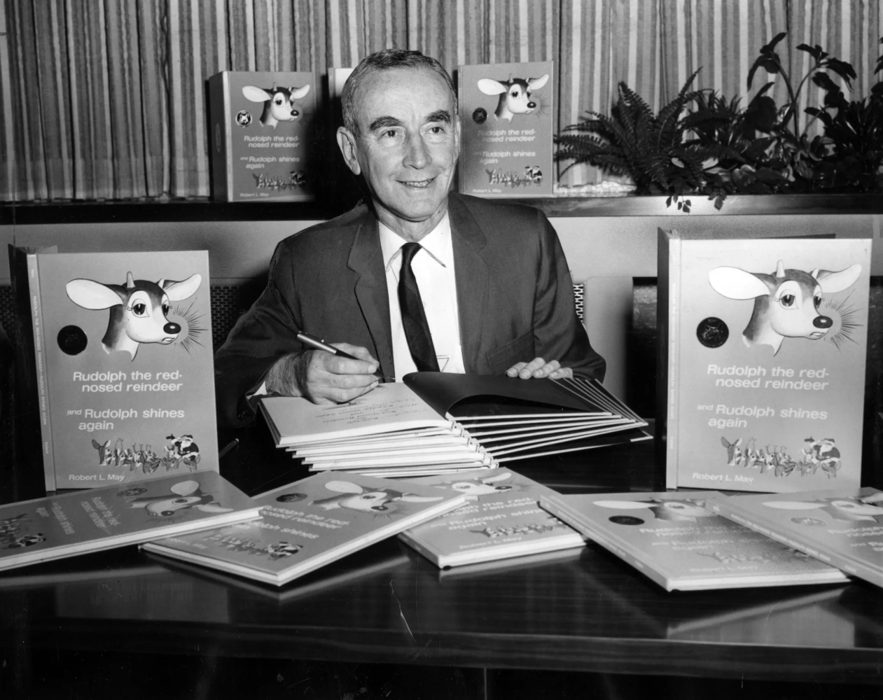 A man in a suit and tie is sitting at a table with books on it