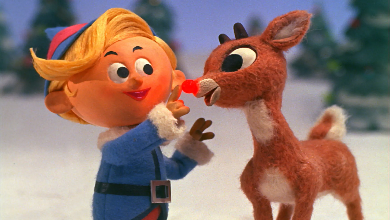 A cartoon elf is putting a red nose on a stuffed reindeer.