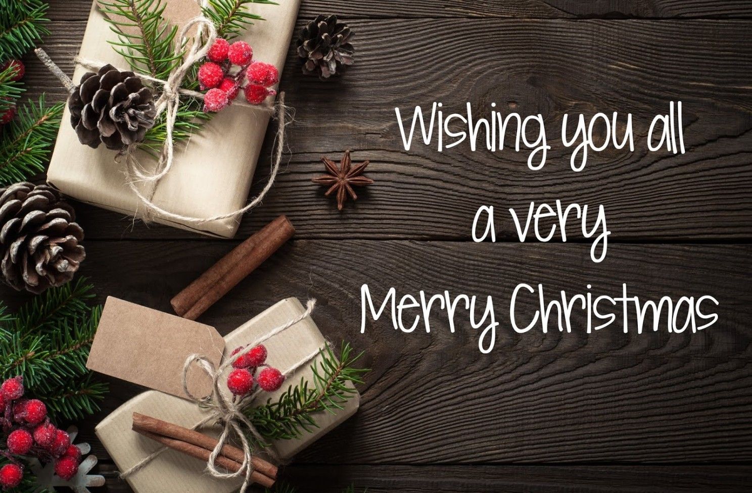 A wooden table topped with christmas decorations and a wishing you all a very merry christmas message.