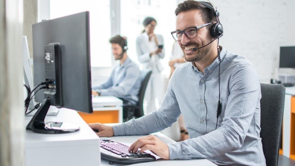 A man wearing a headset is sitting at a desk in front of a computer.