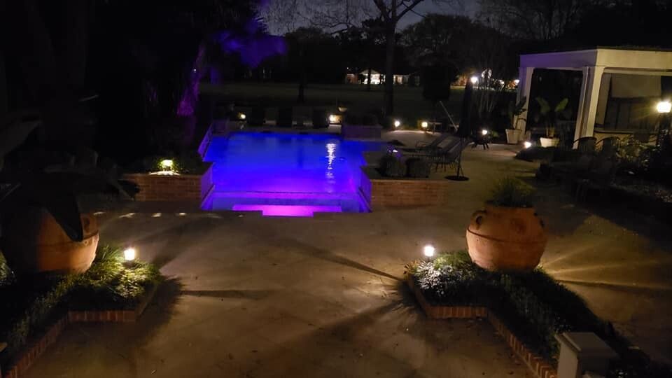 A large swimming pool is lit up at night with purple lights.