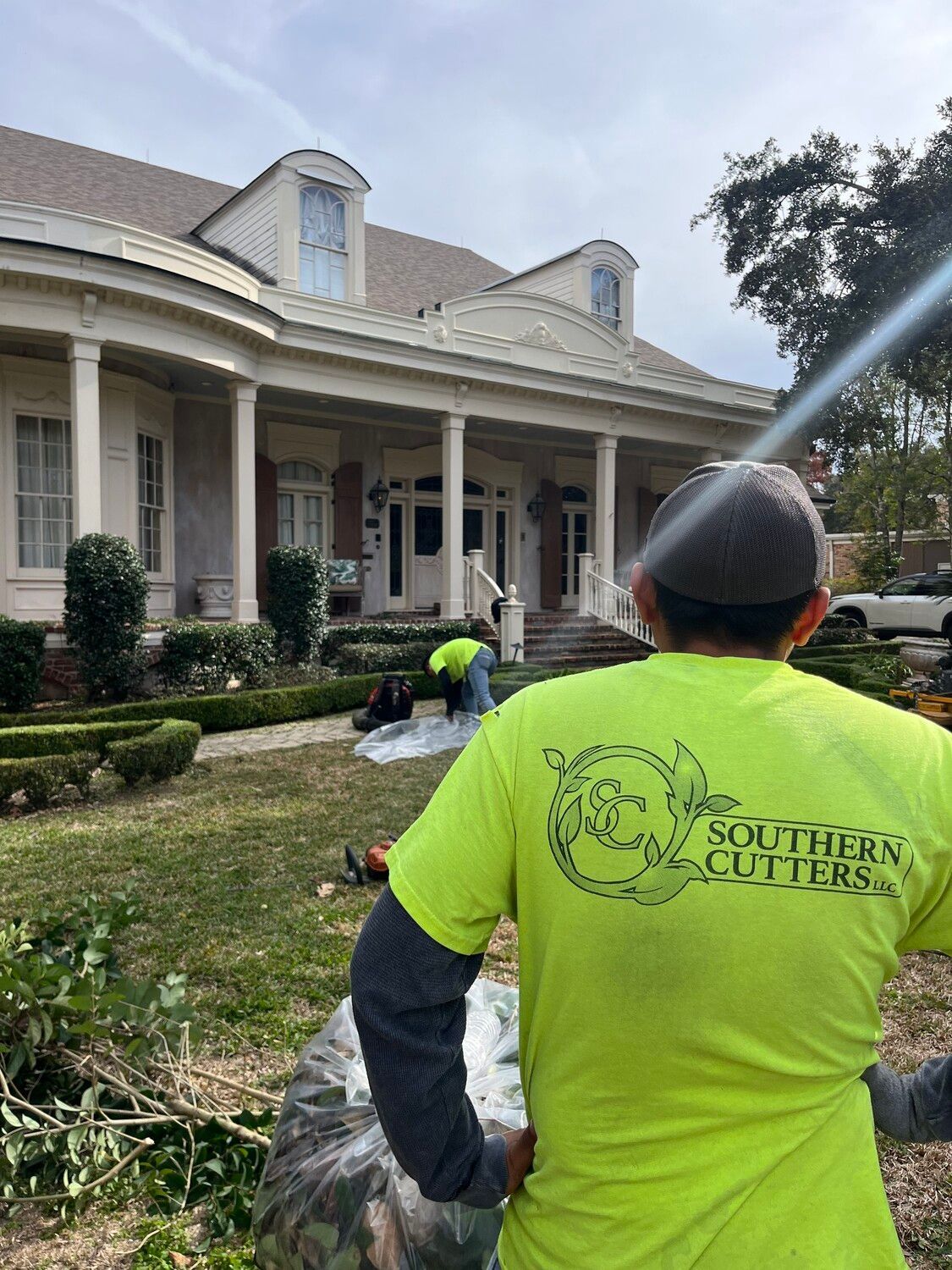 A man in a neon yellow shirt is standing in front of a large house.