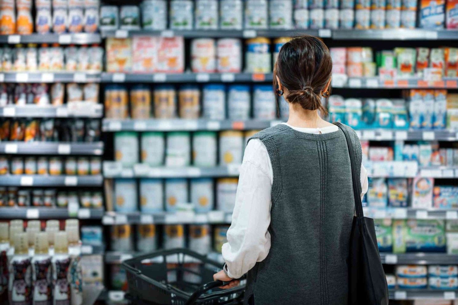 A woman is shopping in a grocery store with a shopping cart.