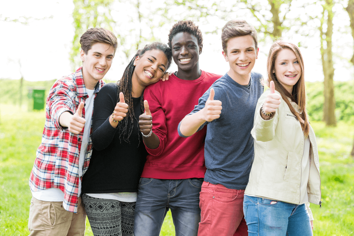 A group of young people are giving a thumbs up in a park.