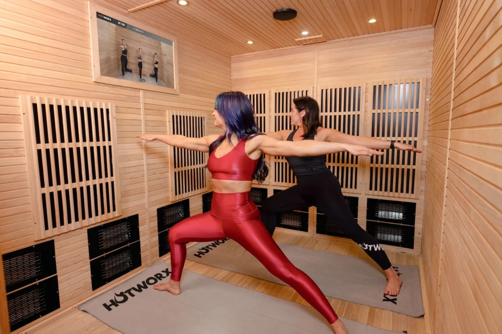 Two people practicing martial arts poses in a wooden training room, one in red and one in black.