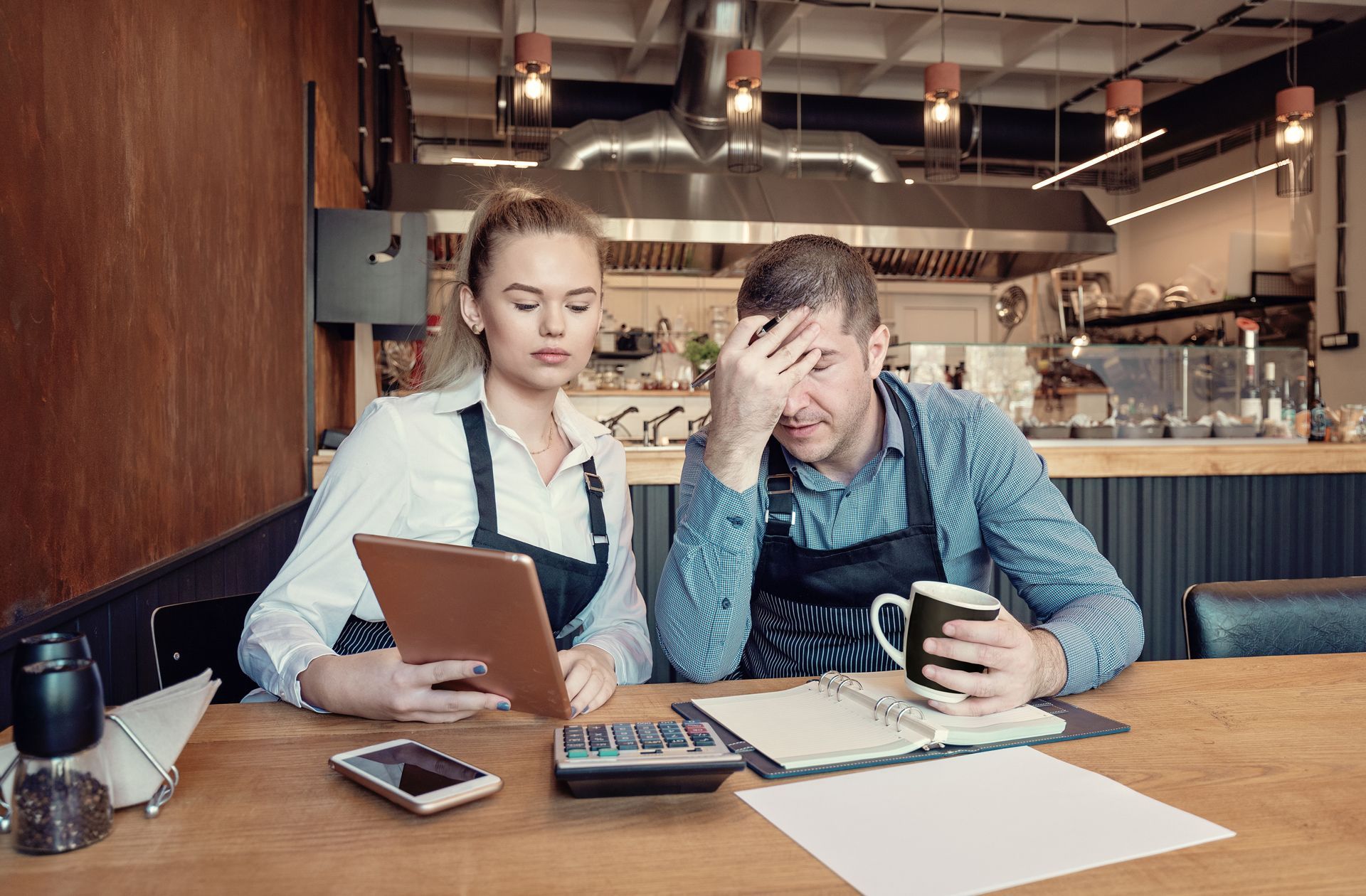 A man and a woman are sitting at a table in a restaurant looking at a tablet.