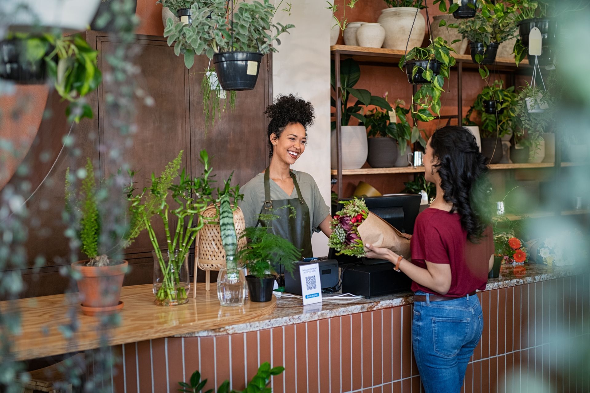 A woman is standing at a counter in a flower shop holding a bouquet of flowers.