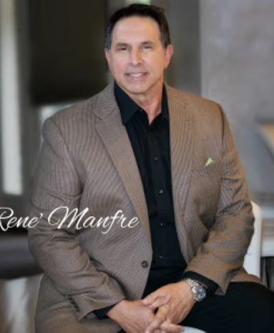 A man in a suit and black shirt is sitting on a couch.