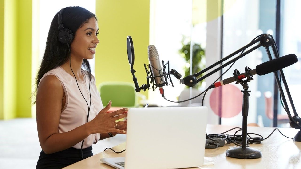 A woman is sitting at a desk with a laptop and a microphone.