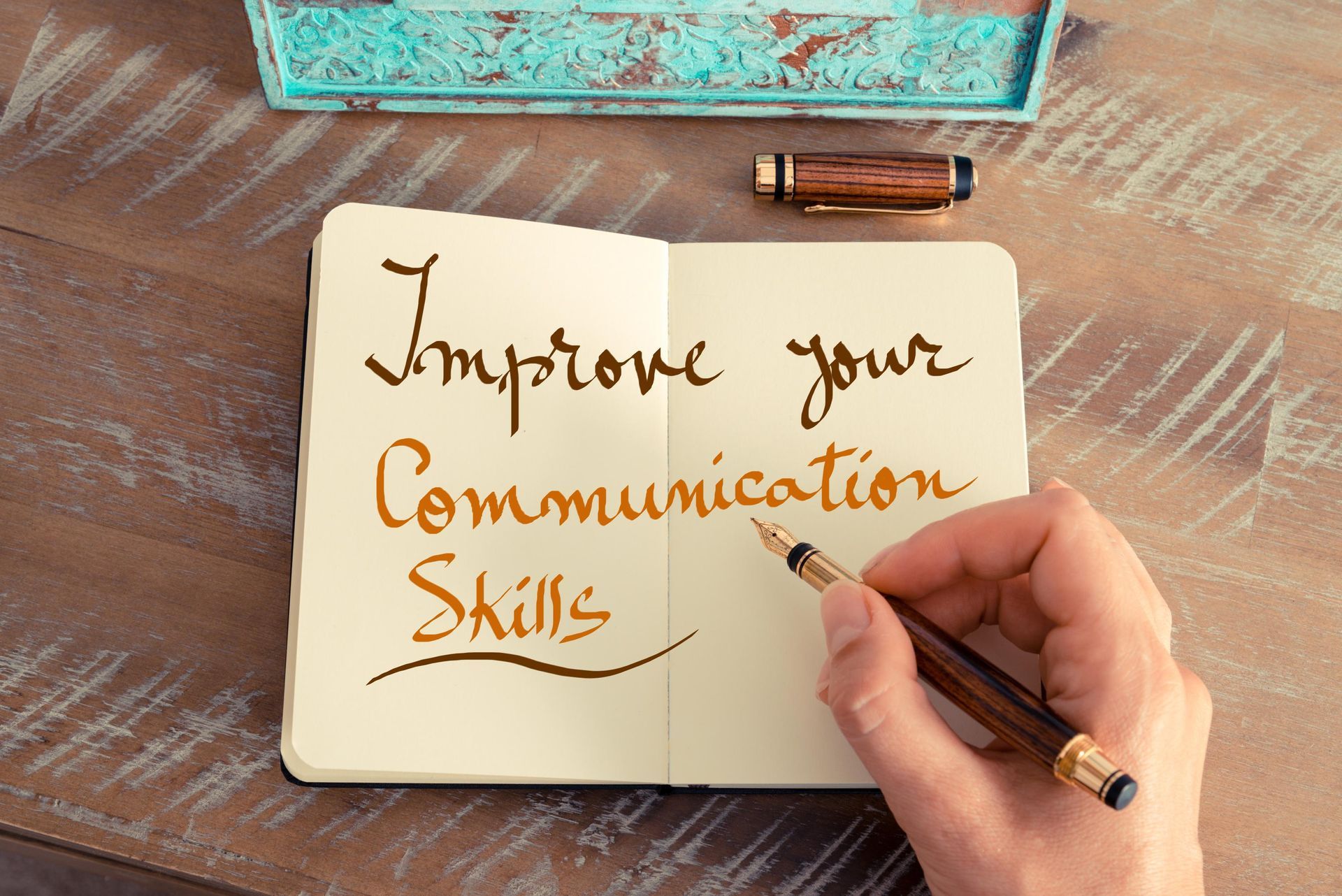 A person is writing in a notebook that says improve your communication skills