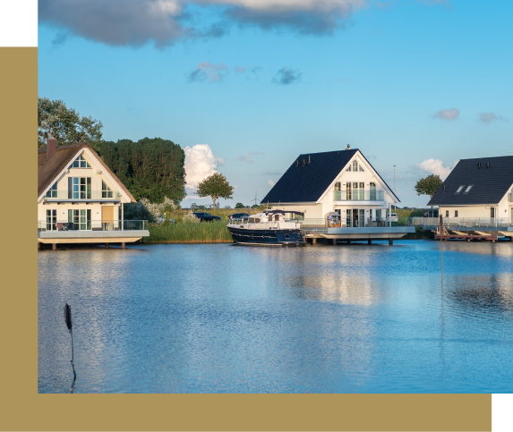 Waterfront homes with boat dock on calm water under a blue sky with fluffy clouds.