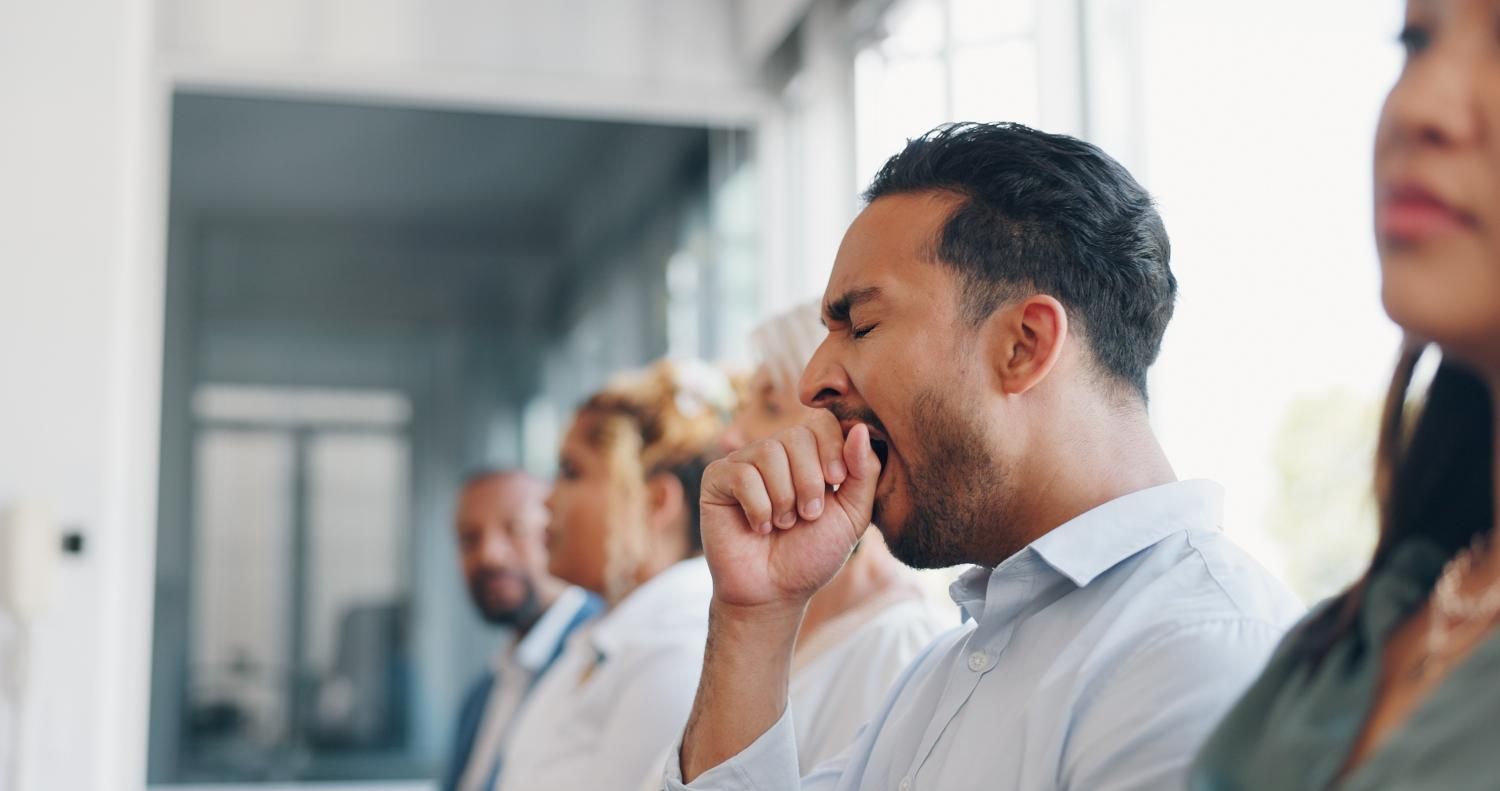 A man is yawning while sitting in a row with other people.