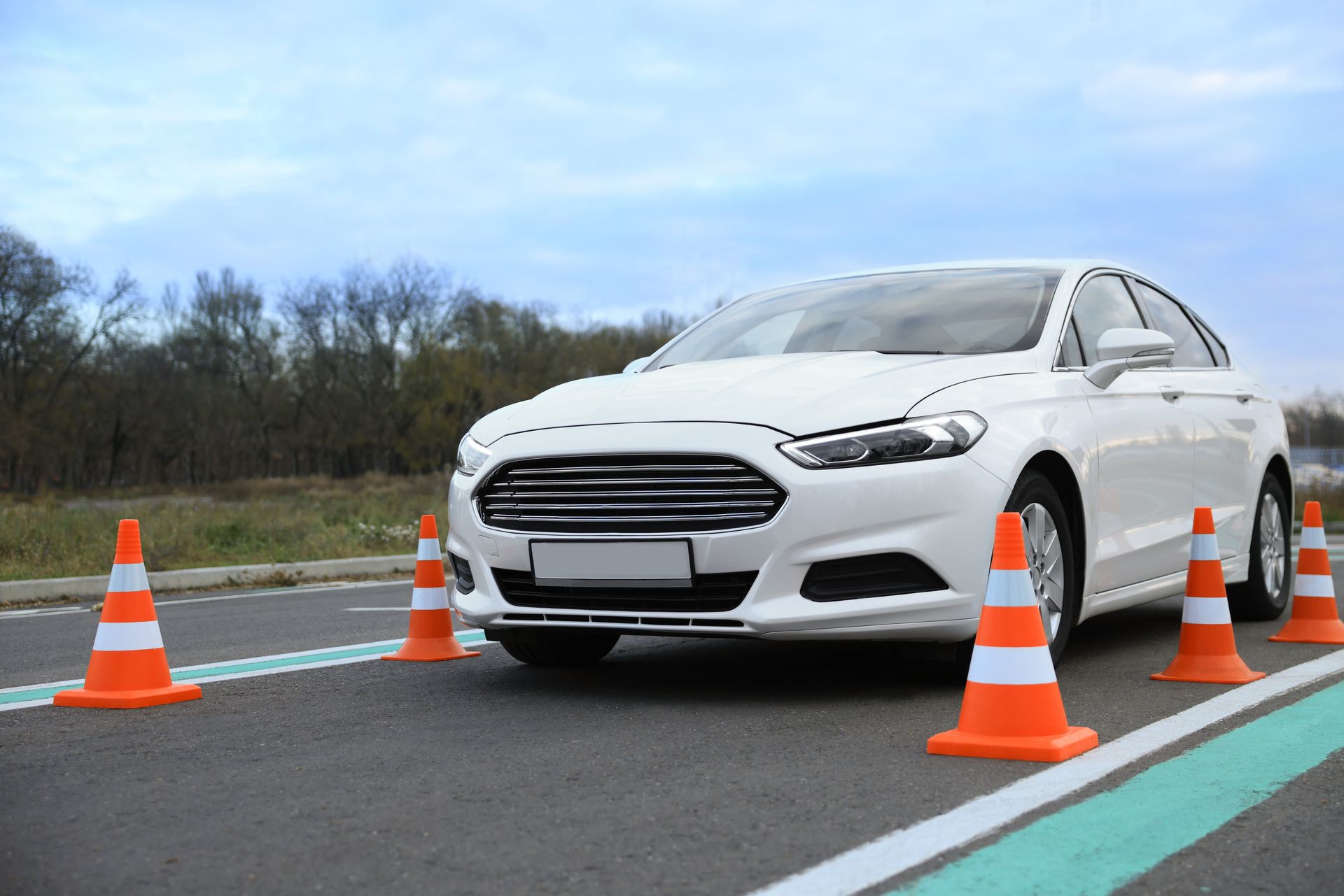 White sedan surrounded by orange cones on a wet road, likely in a driving test or safety course White sedan surrounded by orange cones on a wet road, likely in a driving test or safety course