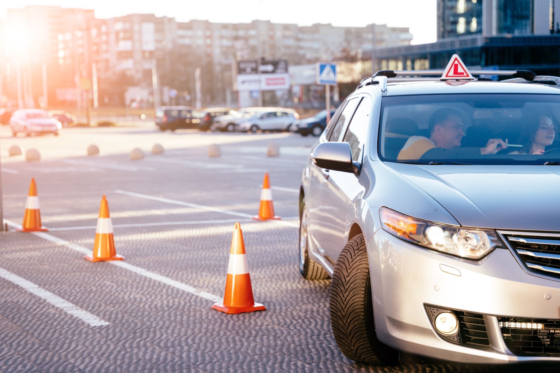 Silver sedan with learner sign driving through orange traffic cones on a city road at sunrise Silver sedan with learner sign driving through orange traffic cones on a city road at sunrise