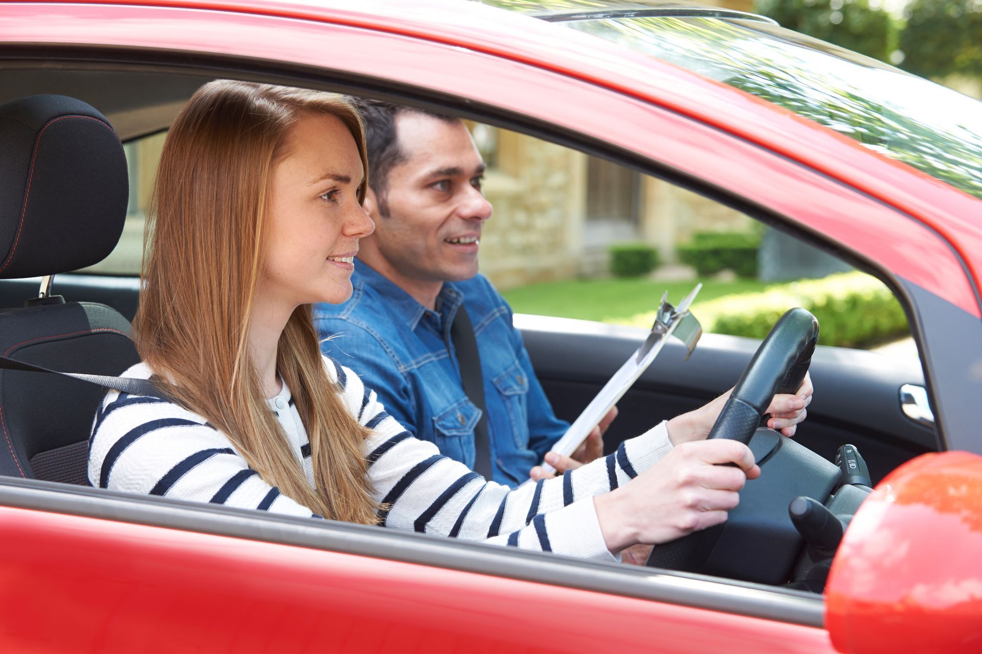 Two people driving a red car, woman at the wheel and man in the passenger seat, both smiling Two people driving a red car, woman at the wheel and man in the passenger seat, both smiling