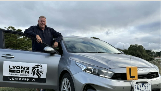 Man standing in a silver driving school car with “Lyon’s Driver Ed” sign on the door Man standing in a silver driving school car with “Lyon’s Driver Ed” sign on the door