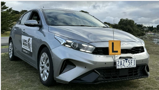 Silver learner car on grass with yellow L plate and side decals outdoors Silver learner car on grass with yellow L plate and side decals outdoors