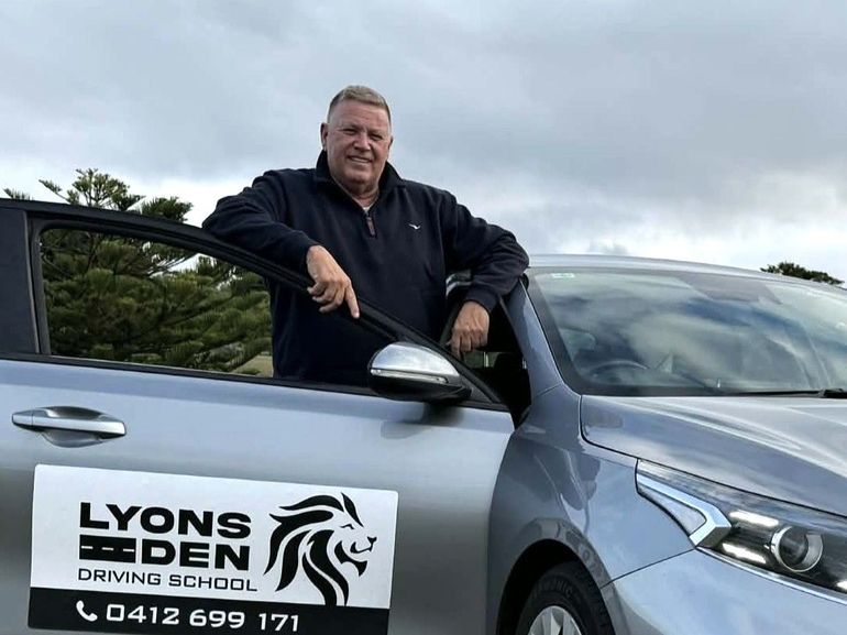 Man leaning on open silver car door with Lyons Eden driving school sign on side Man leaning on open silver car door with Lyons Eden driving school sign on side