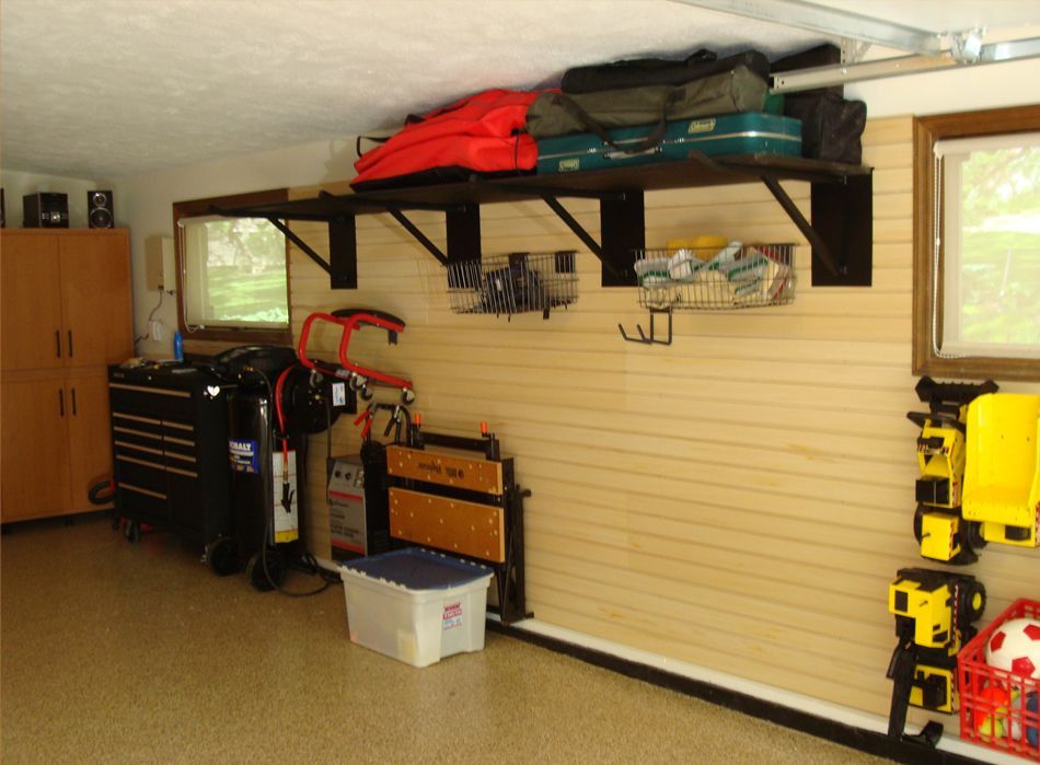 Garage interior with storage shelves, tools, and cabinets against beige slat wall.