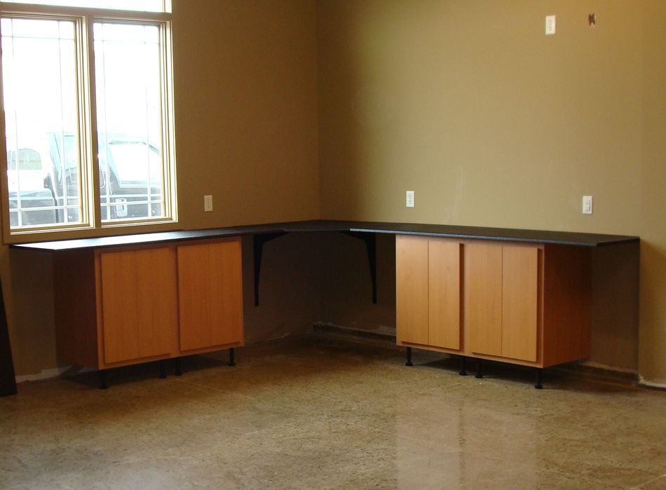 Corner workspace with brown cabinets, black countertop, and a window.