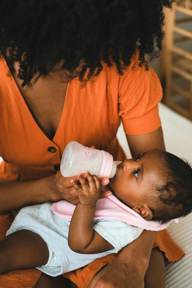 Woman in orange dress feeding a baby with a bottle on her lap