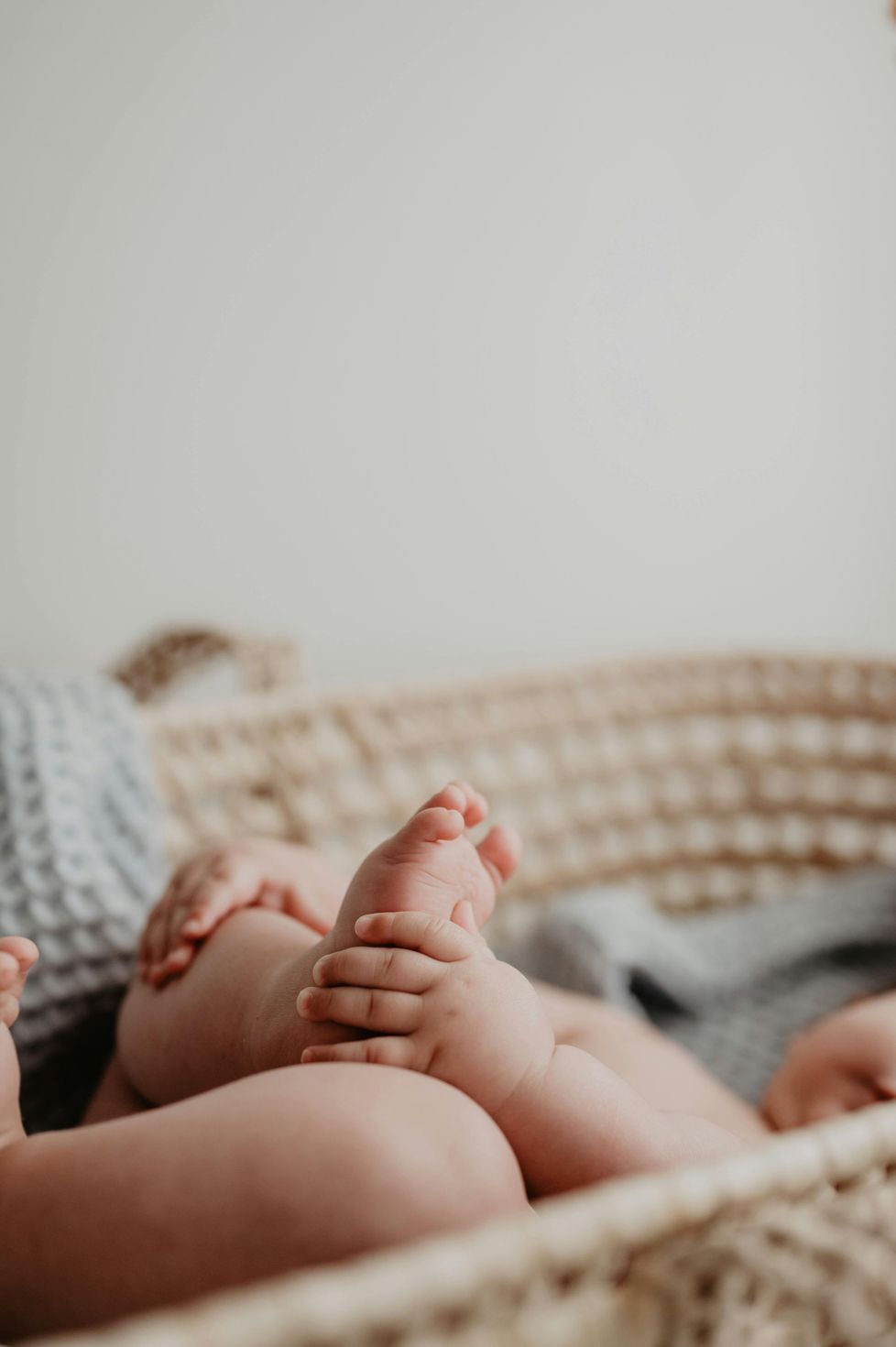 Newborn feet resting in a woven basket with a soft blanket background