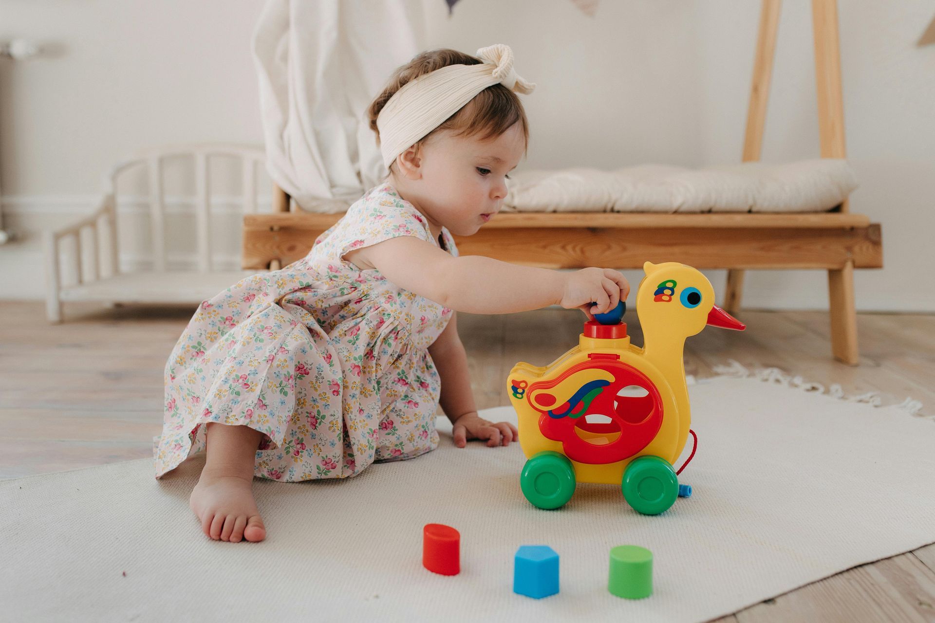 Toddler playing with a colorful toy duck on a rug, with building blocks nearby.