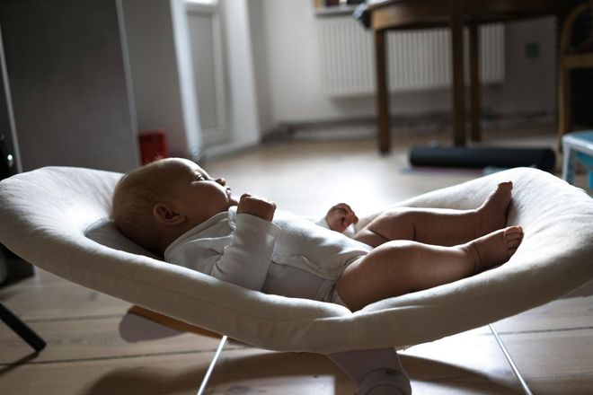 Sleeping baby in a white bouncer in a bright room