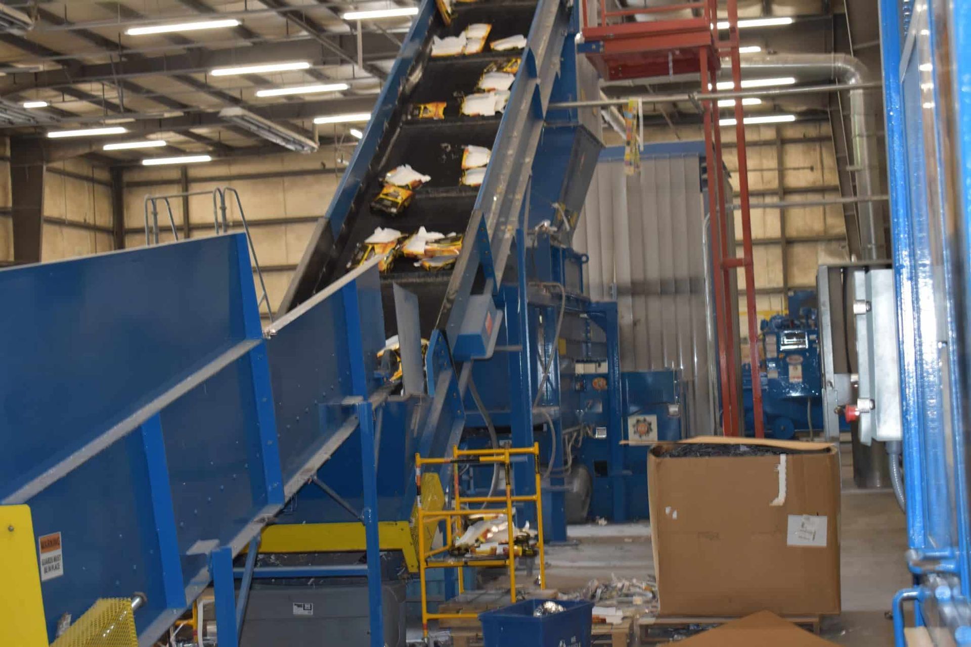 Blue recycling facility machinery sorts materials; boxes on conveyor belt.