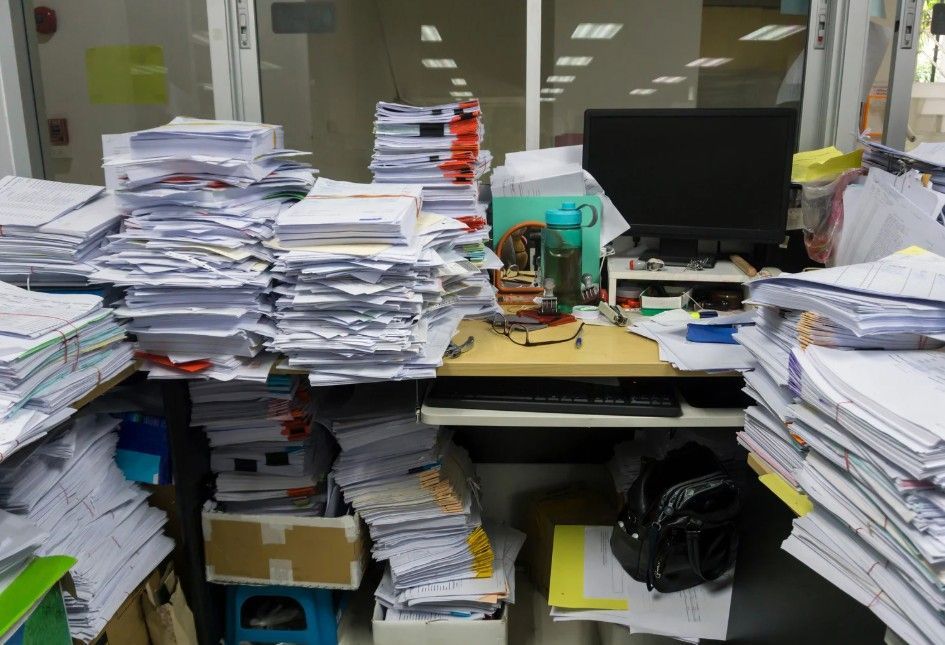 Desk overloaded with stacks of papers and office supplies.