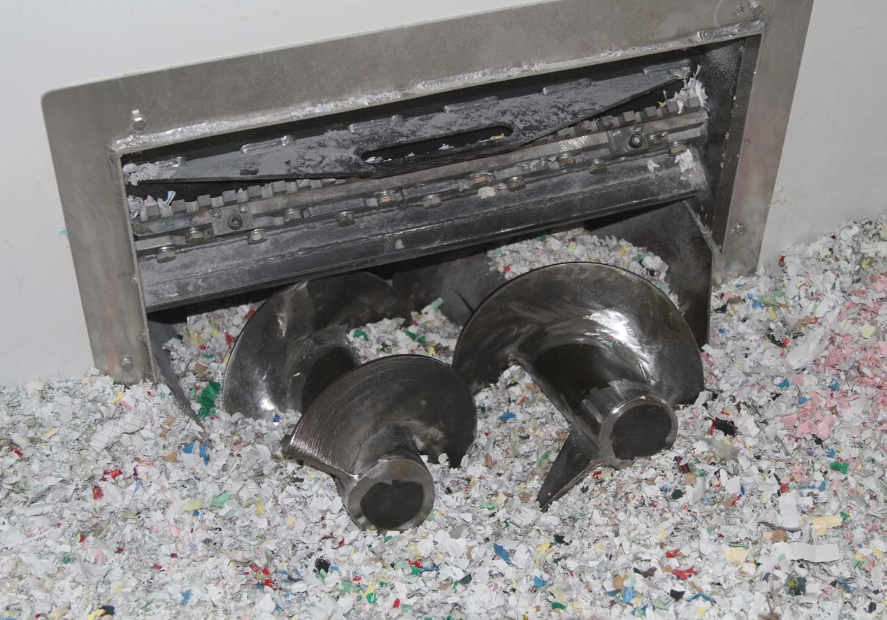Shredding machine with internal blades, shredding plastic into small colorful pieces.