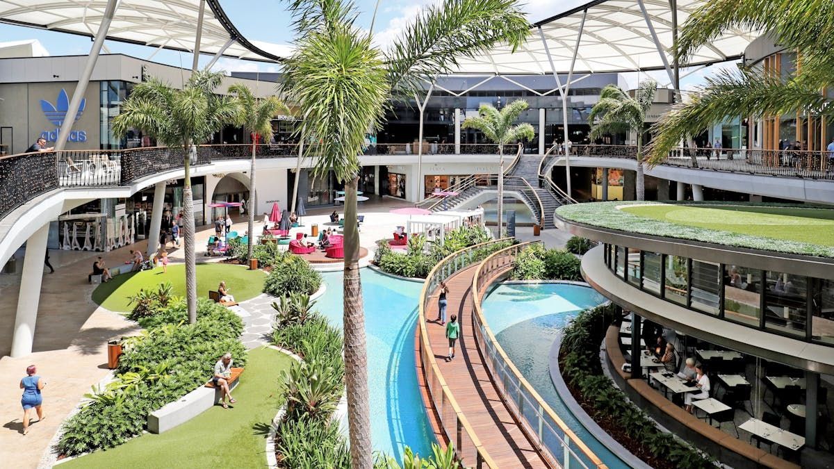 Shopping center com passarelas, lojas, áreas verdes e uma fonte.