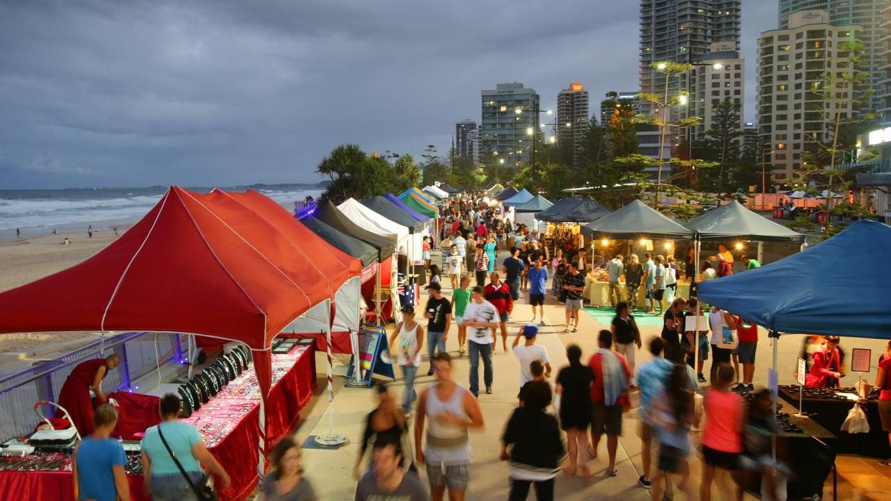 Mercado à beira-mar com muita gente, barracas e arranha-céus ao fundo ao entardecer.