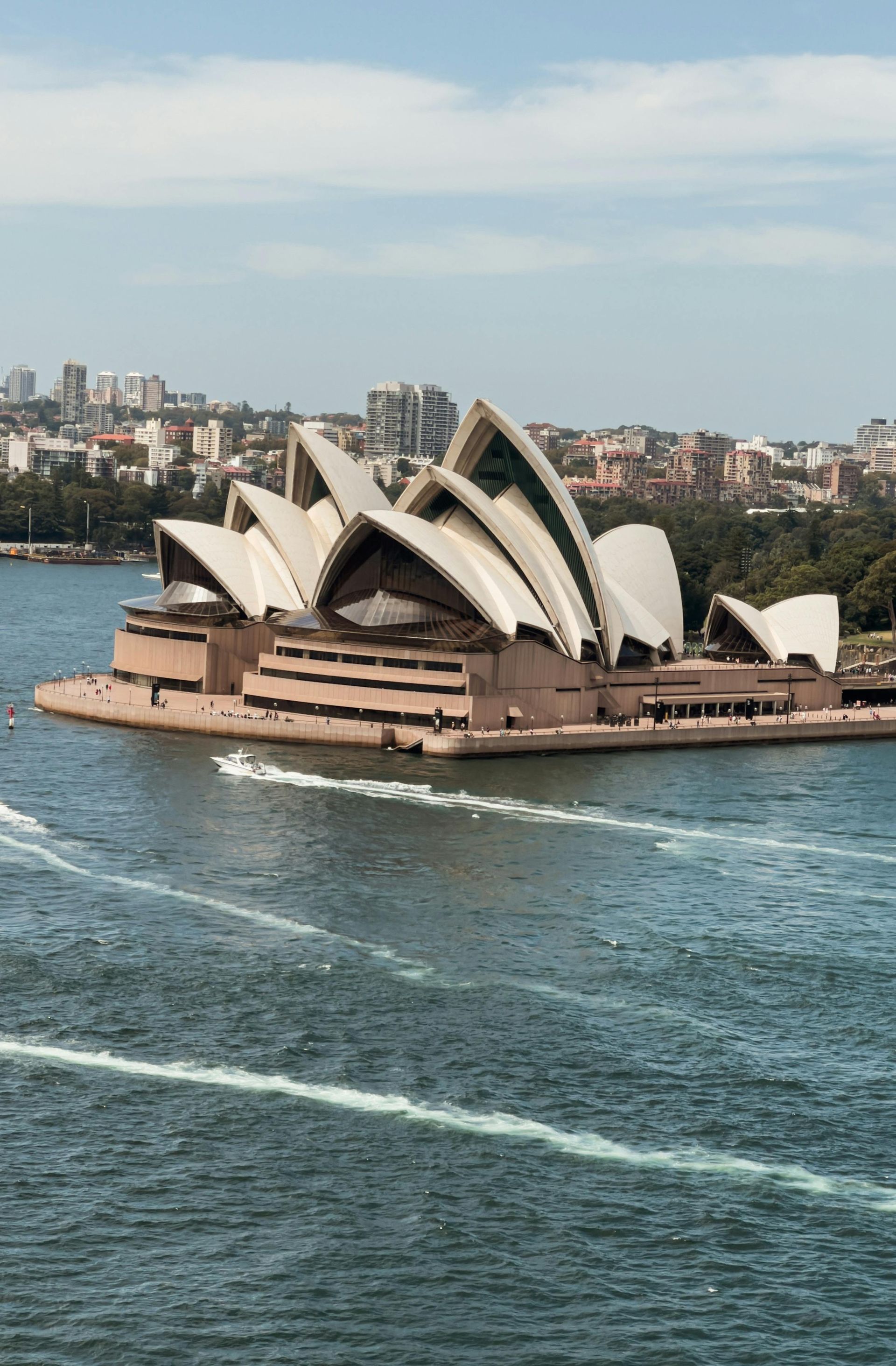A Ópera de Sydney no porto, conchas brancas contra o horizonte da cidade, água azul.