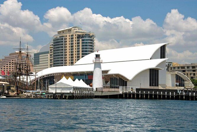 Museu Marítimo de Sydney, edifício moderno branco com farol, no porto, céu nublado.