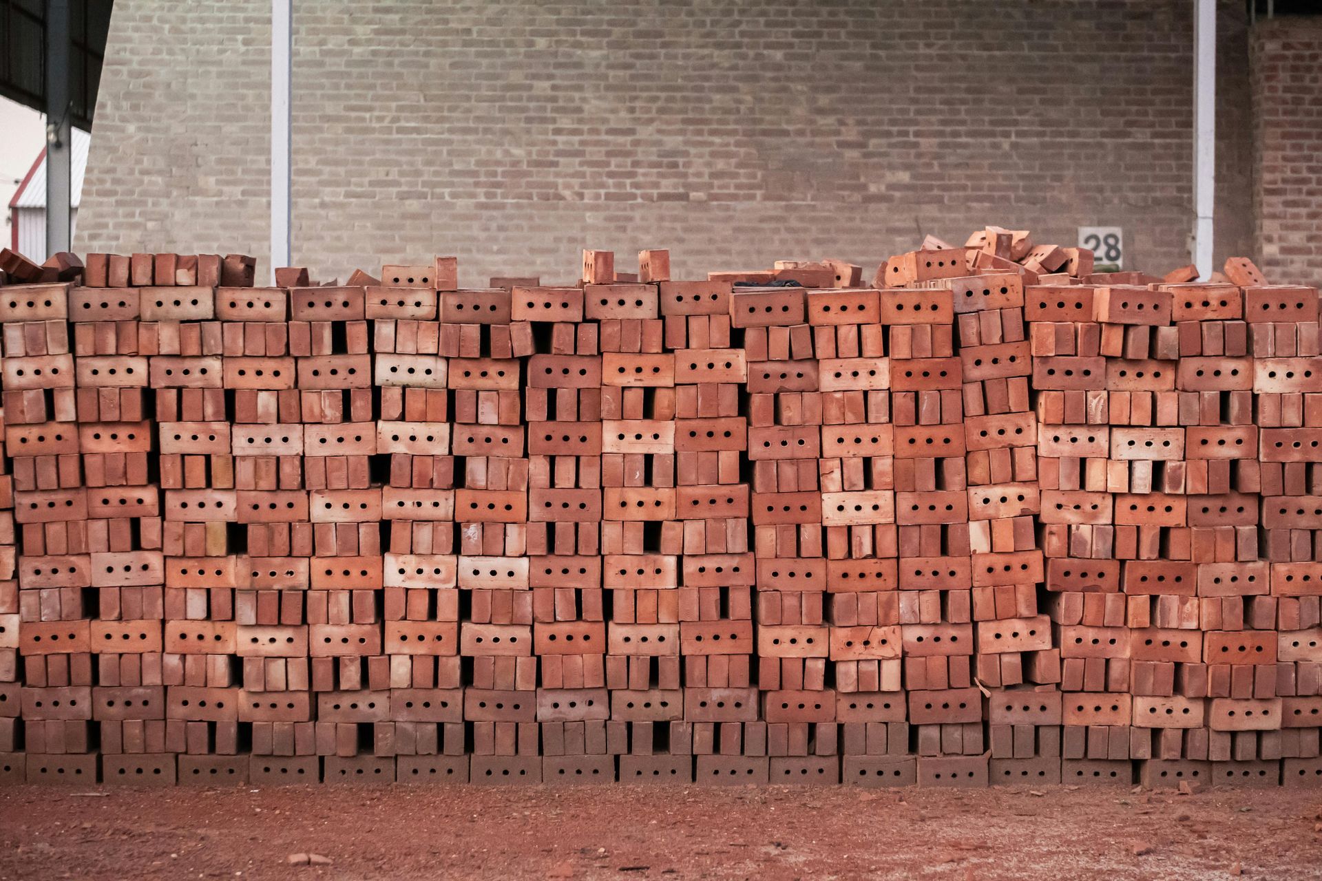 Pile of red bricks stacked in front of a brick wall inside a building.