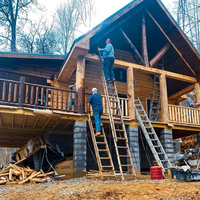 A man on a ladder is working on a log cabin