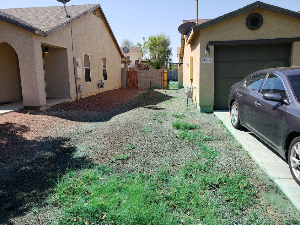 Narrow side yard between two houses with gravel, grass, and a parked car beside a garage.