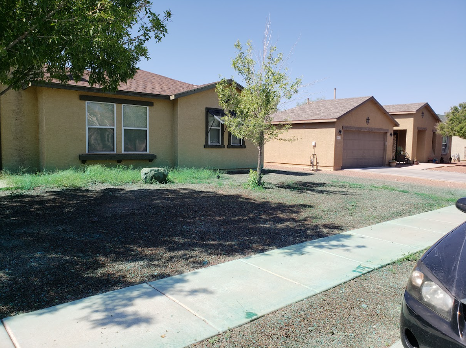 Suburban house with front yard, driveway, and parked car under a clear blue sky