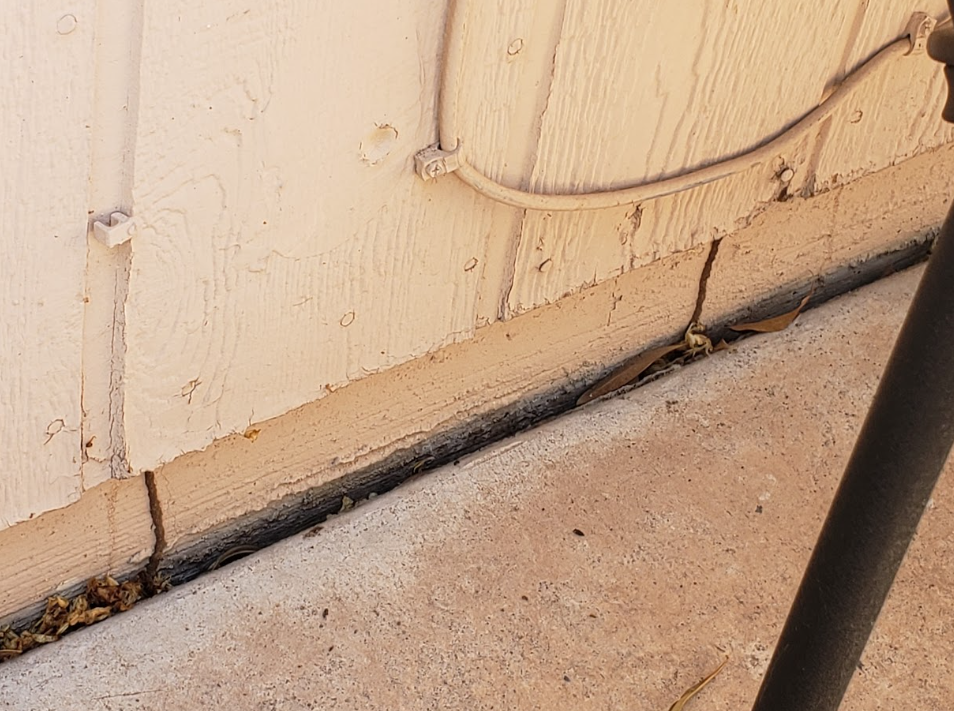 Cracked beige wall by concrete floor with exposed cable and black pole edge