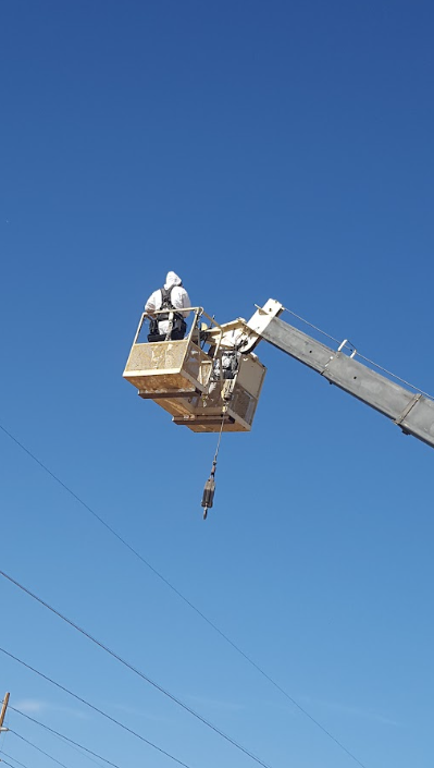 Utility workers in a bucket lift servicing power lines against a clear blue sky