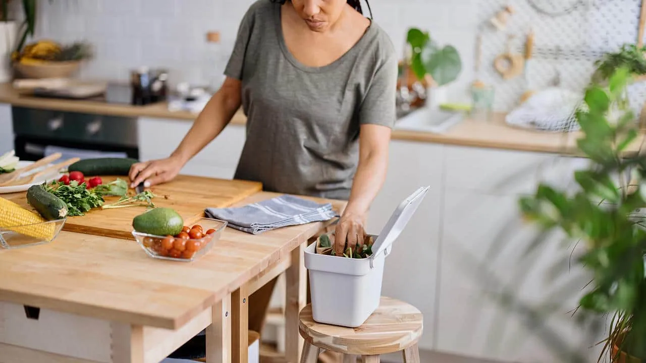 A woman is cutting vegetables on a wooden cutting board in a kitchen.