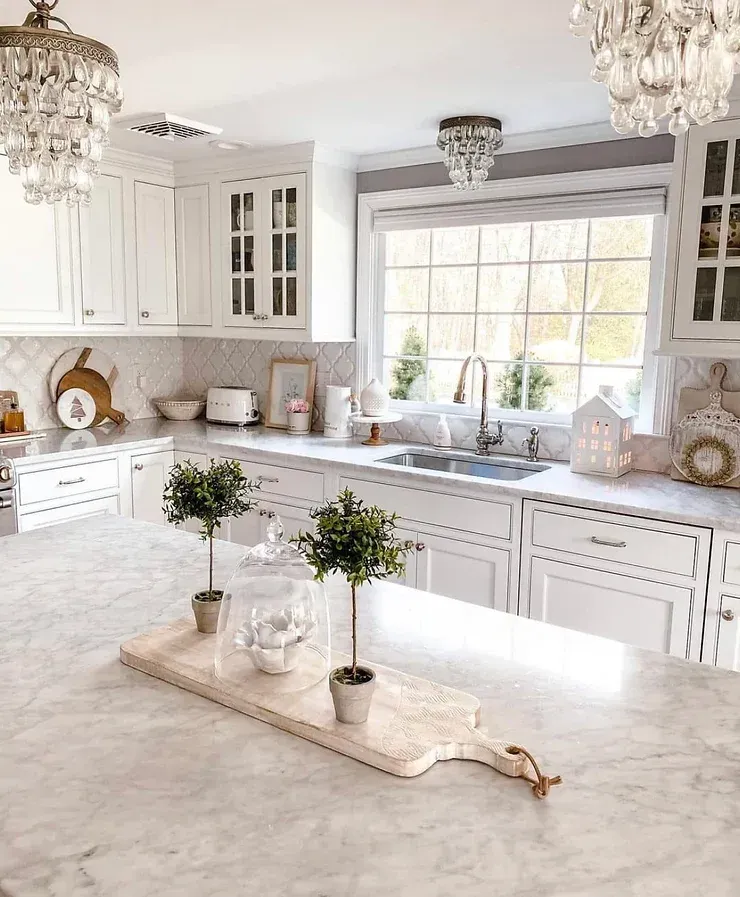 A kitchen with white cabinets , marble counter tops , a sink , and a window.