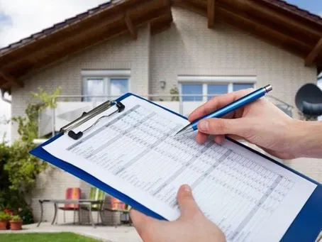 A person is writing on a clipboard in front of a house
