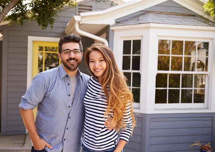 A man and a woman are standing in front of a house.