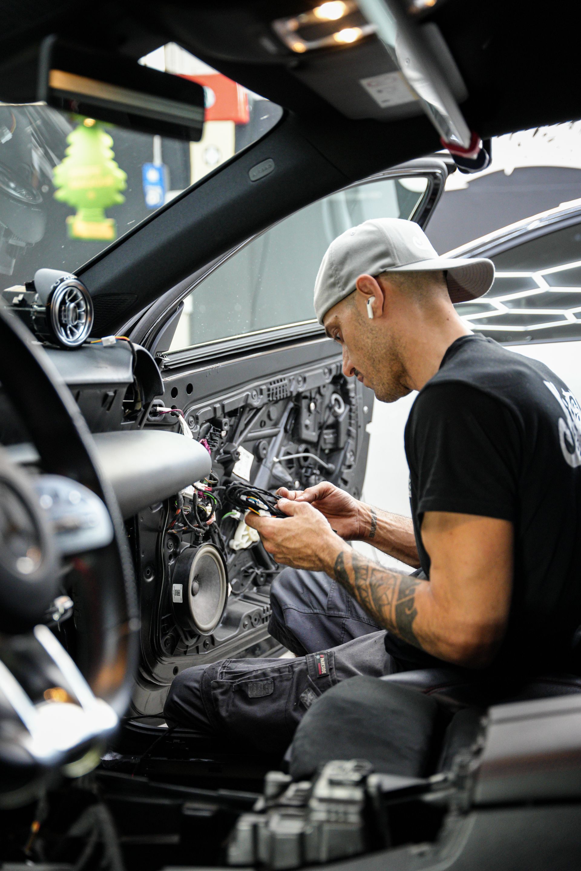 Meccanico al lavoro all'interno dell'abitacolo di un'auto Mercedes con i pannelli del cruscotto rimossi.