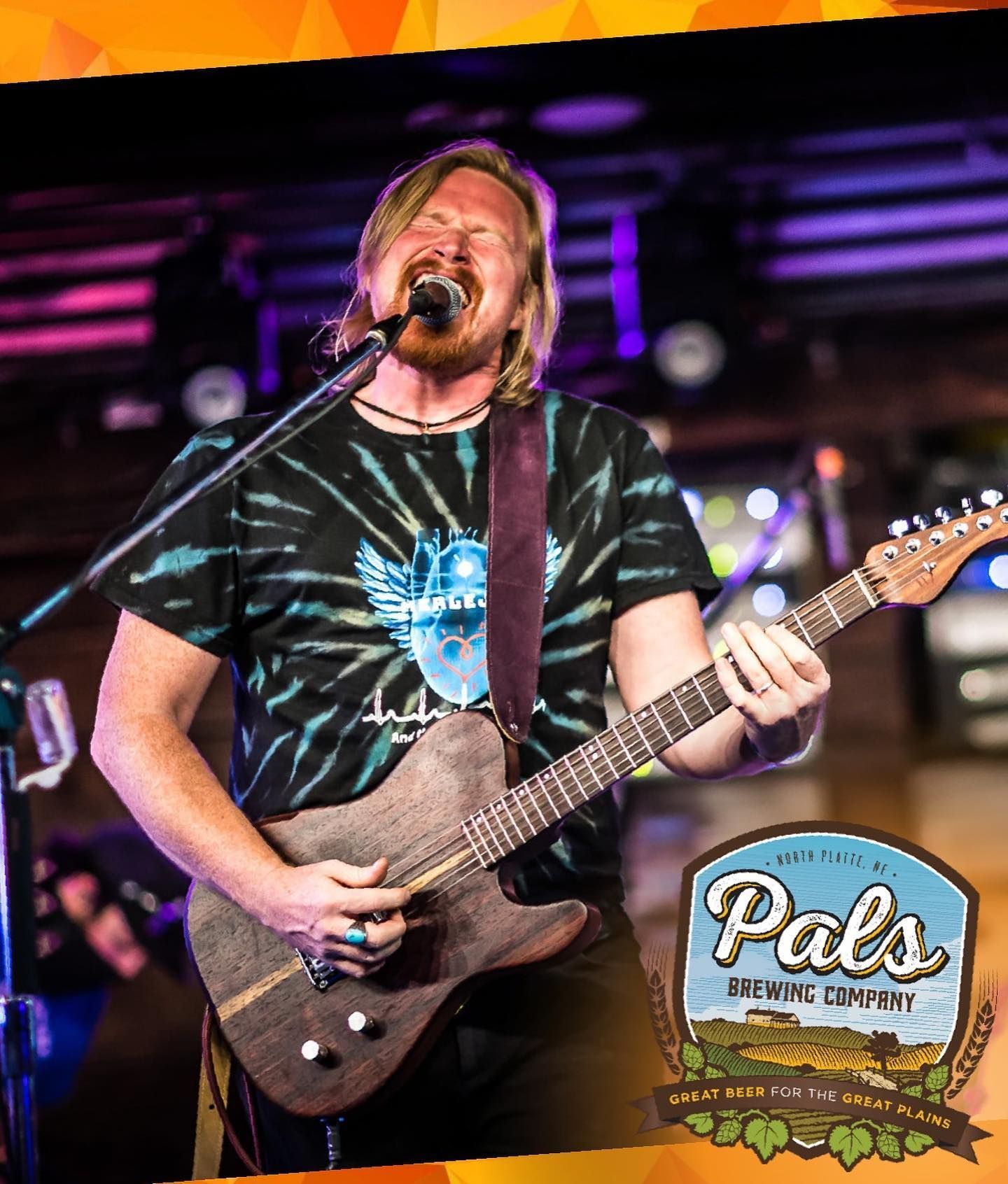 Man playing guitar and singing on stage at Pals Brewing Company.